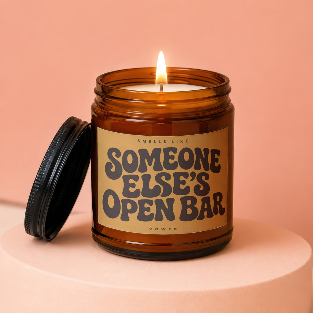 Amber candle with lit wick and lid off, reads "Smells Like Someone Else's Open Bar".