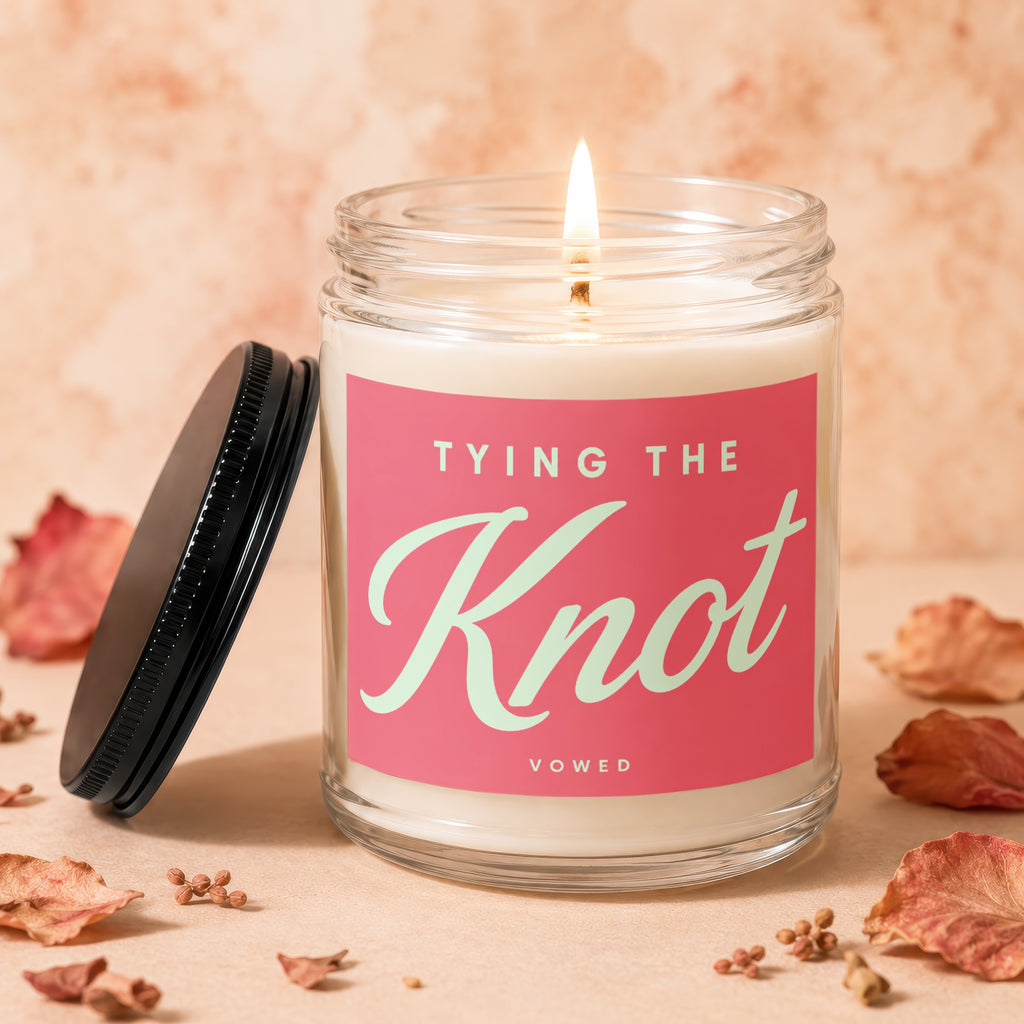 Glass candle with lit wick, pink label reads "TYING THE Knot, VOWED".