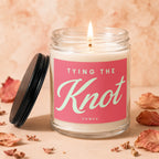 Glass candle with lit wick, pink label reads "TYING THE Knot, VOWED".