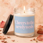Glass candle with lit wick and lid asks "Cheers to the newlyweds."