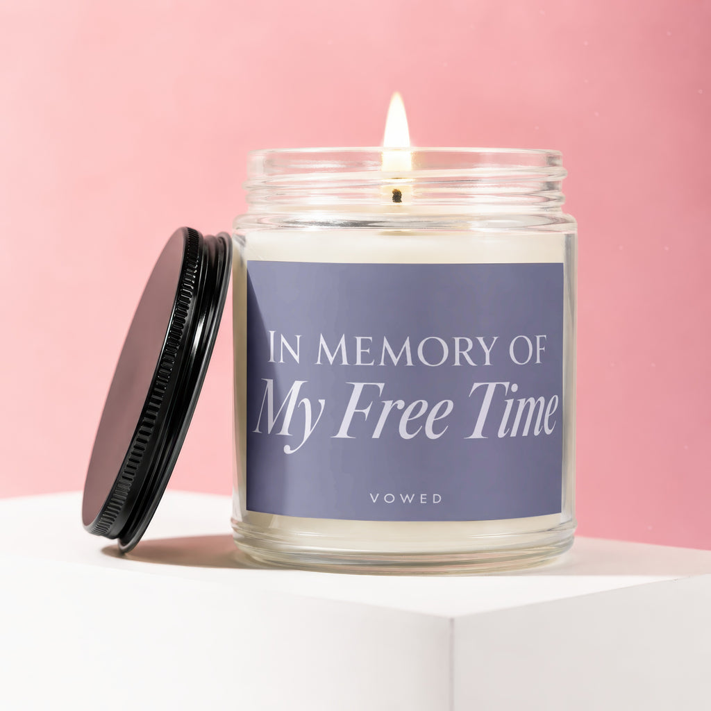 Glass candle with lit flame, "In Memory Of My Free Time" text on label.