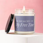 Glass candle with lit flame, "In Memory Of My Free Time" text on label.