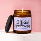 Amber jar candle with lit wick and black lid, displays "Smells like Official Spellcaster" text.