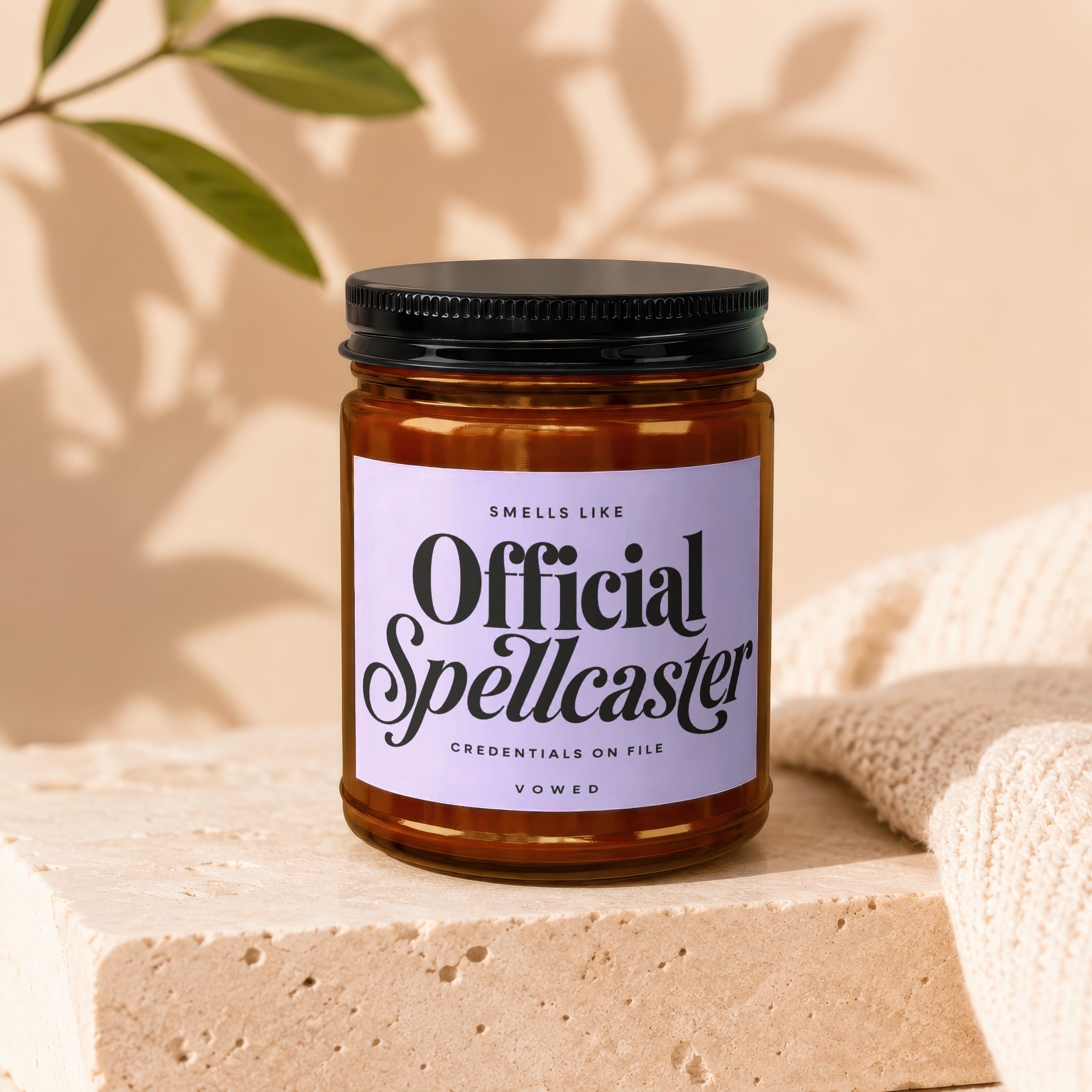 Amber jar candle with black lid featuring "Official Spellcaster" text on lavender label.