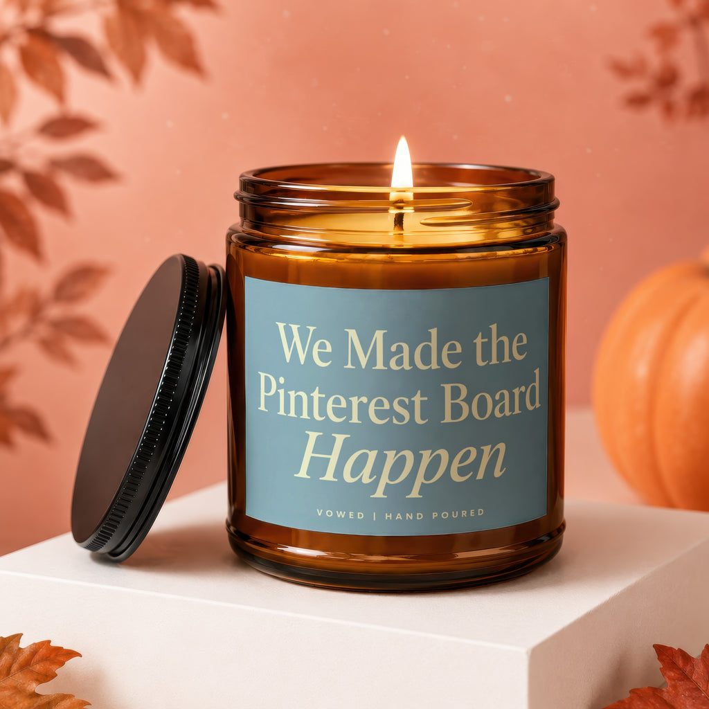 Brown glass candle with lit wick, blue label reads "We Made the Pinterest Board Happen".