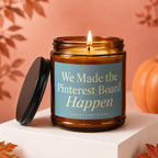 Brown glass candle with lit wick, blue label reads "We Made the Pinterest Board Happen".