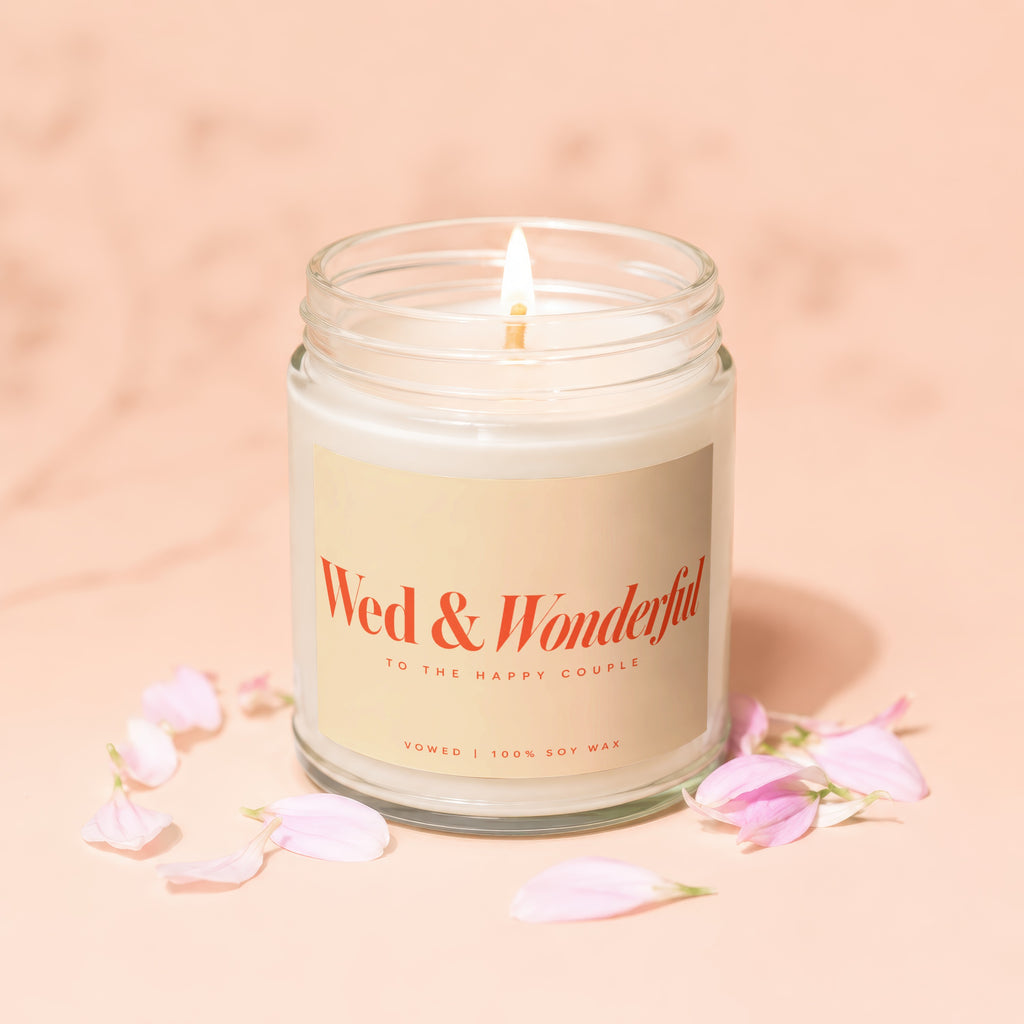 Burning soy wax candle with "Wed & Wonderful" label, surrounded by pale pink petals.