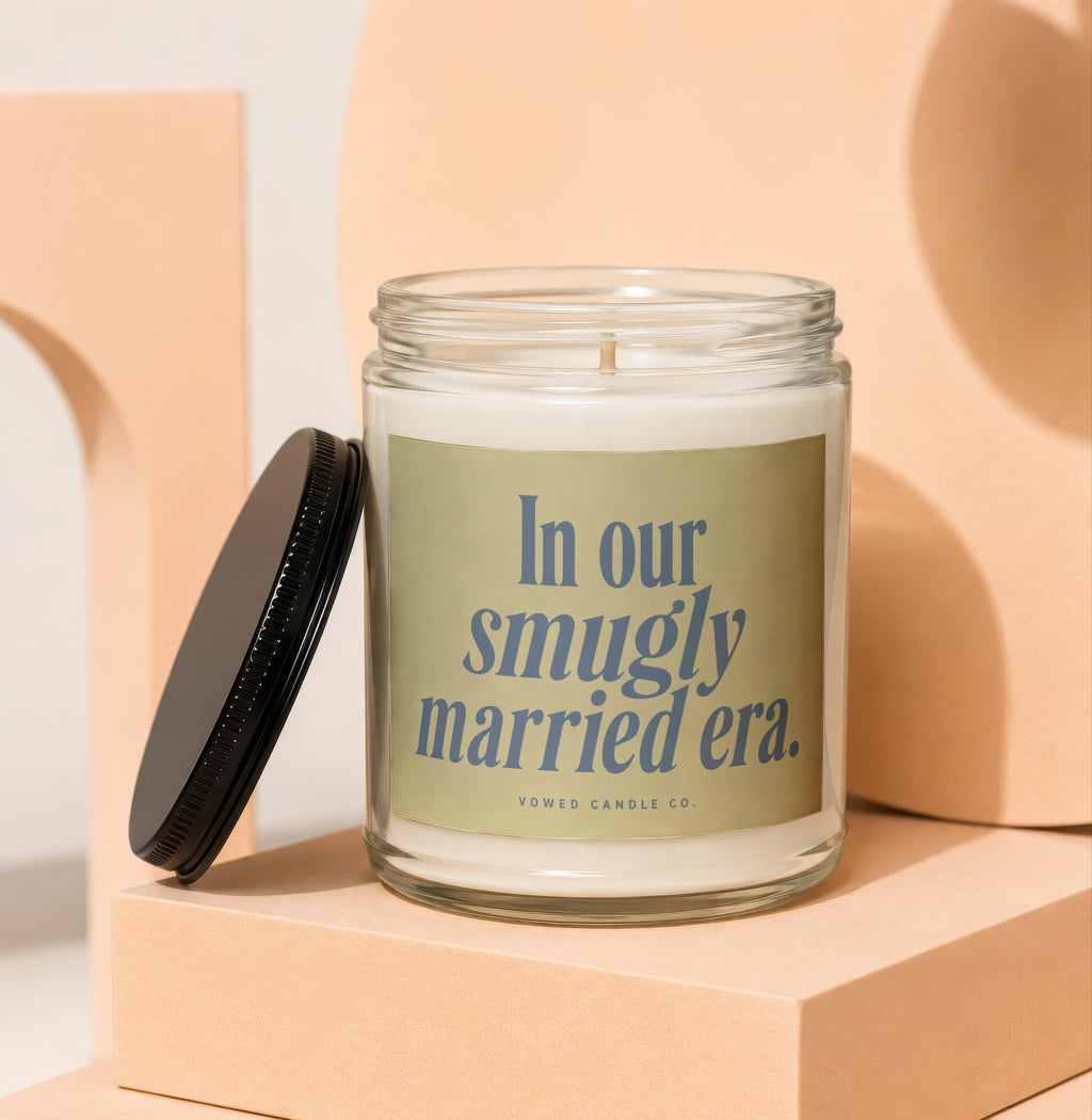 Glass candle with a black lid and label reading "In our smugly married era."