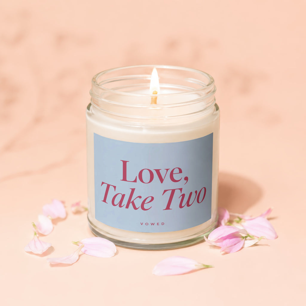 Lit candle with "Love, Take Two" text on a blue label and pink petals.