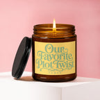 Amber candle with lit wick, yellow label reading "Our Favorite Plot Twist VOWED".