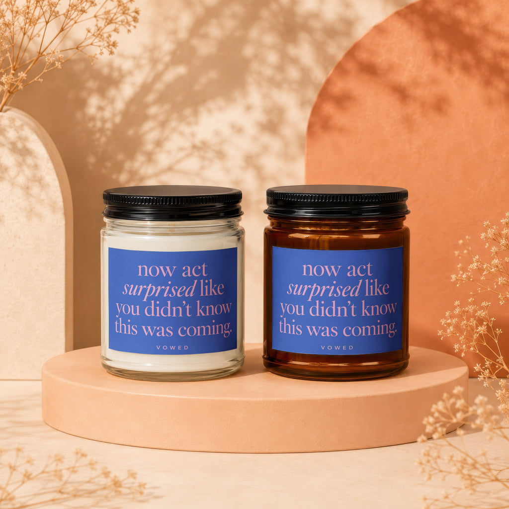 Two scented candles with blue labels featuring pink text: "now act surprised like you didn't know this was coming."
