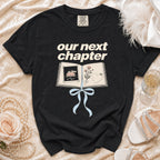 Black t-shirt with "our next chapter" text and an open book graphic.