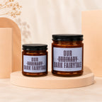 Two amber glass candles with black lids and "Our Ordinary Dark Fairytale" labels.