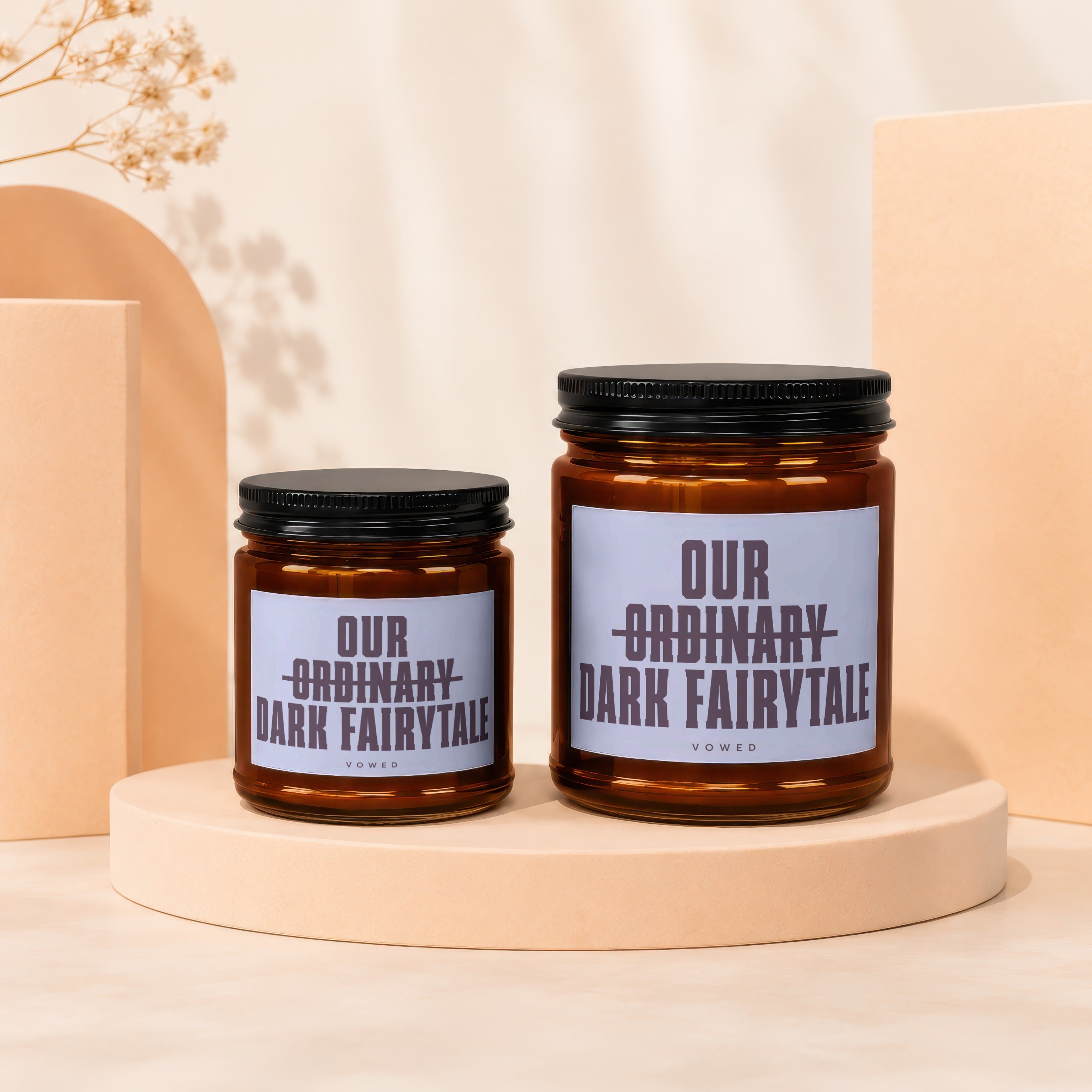 Two amber glass candles with black lids and "Our Ordinary Dark Fairytale" labels.