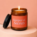 Keeper of Secrets amber glass candle with lit flame and black lid.