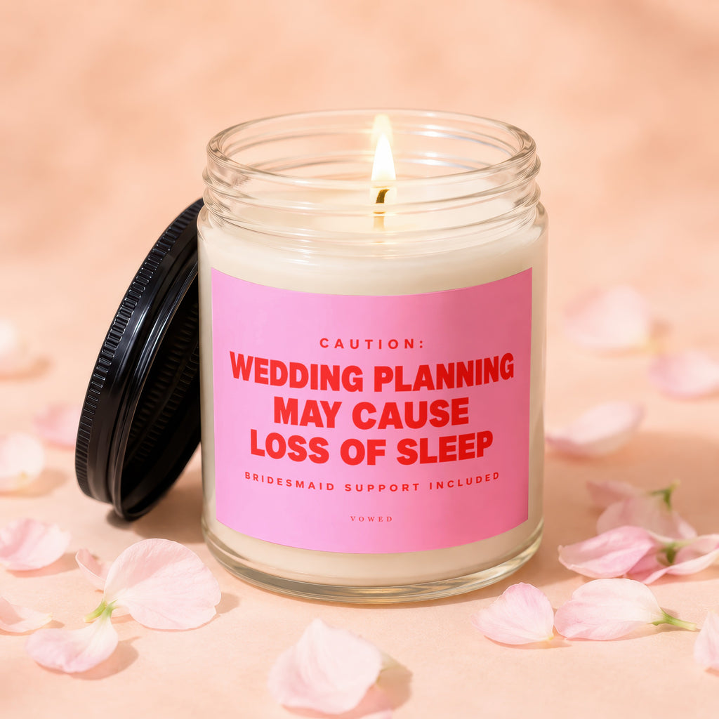Glass candle with pink label reading "CAUTION: WEDDING PLANNING MAY CAUSE LOSS OF SLEEP"