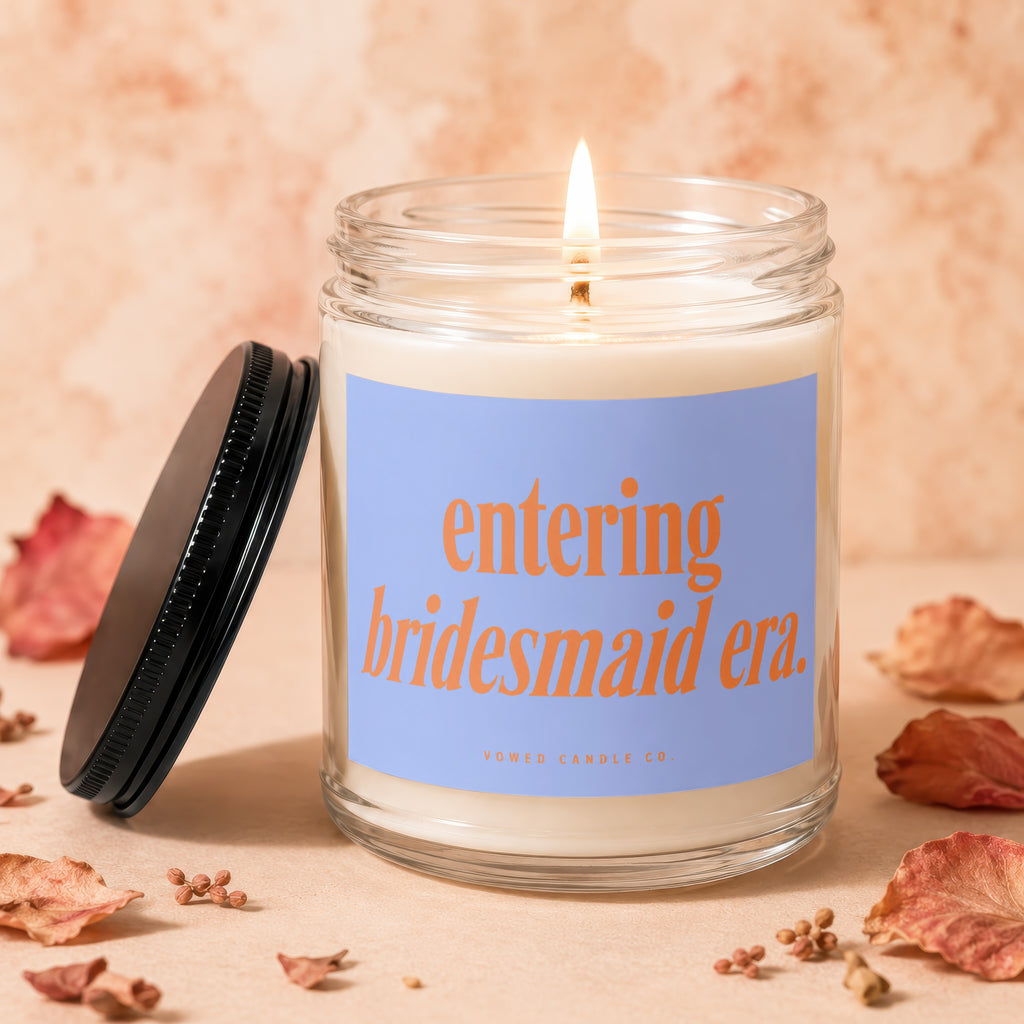 Lit candle with a blue label that reads "entering bridesmaid era. VOWED CANDLE CO."