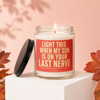 Glass candle with lit wick, featuring red label with gold text "Light this when my son is on your last nerve".
