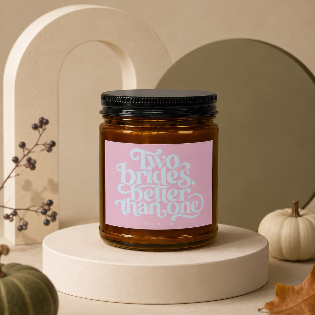 Amber glass candle with pink label reading "Two Brides, Better Than One"