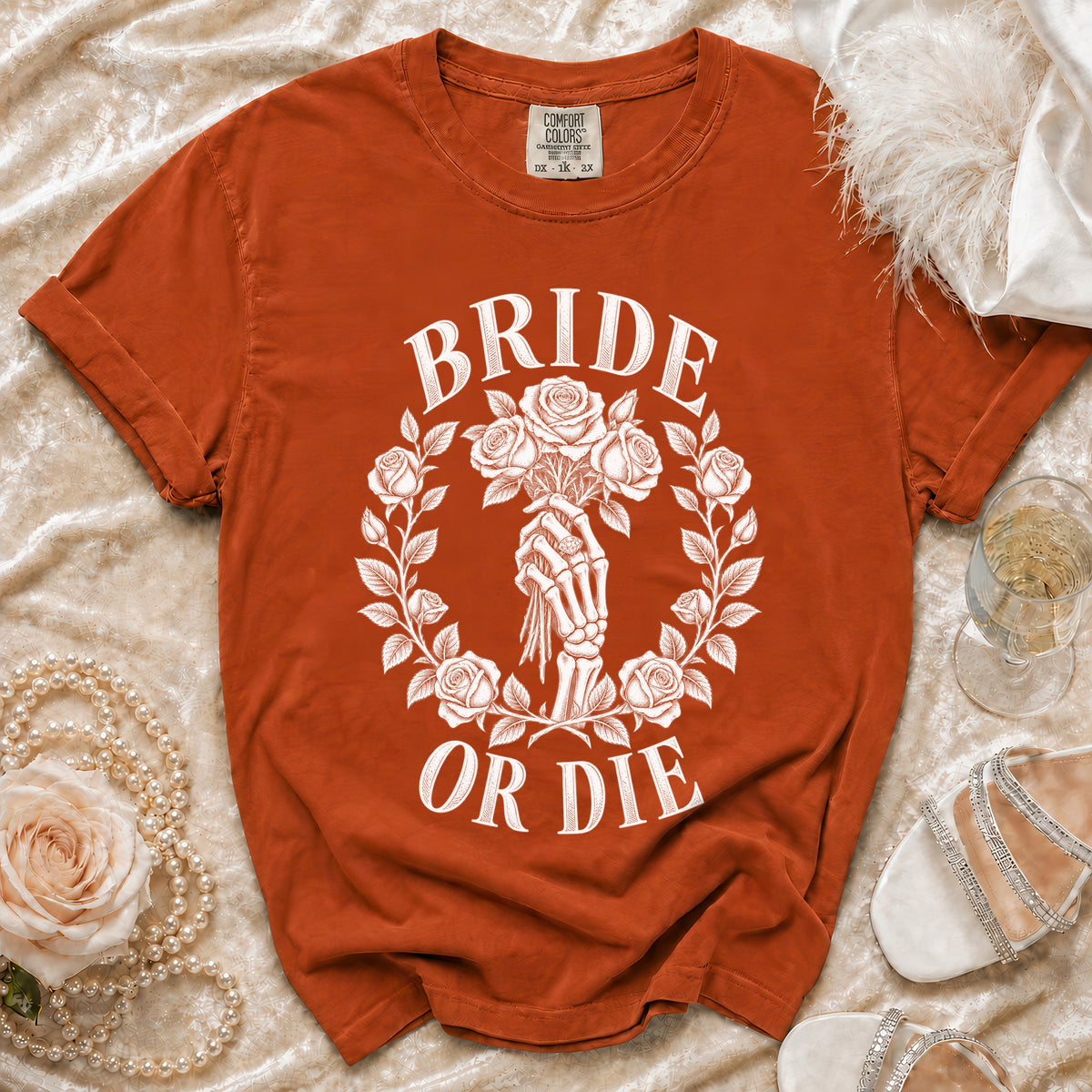 Orange t-shirt with white graphic of skeleton hand holding roses, text "BRIDE OR DIE".