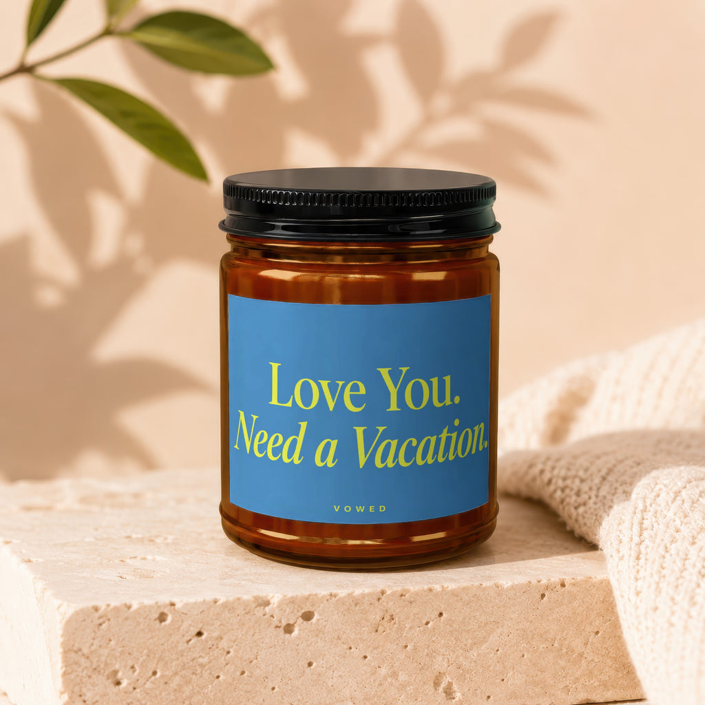 Amber glass candle with blue label reading "Love You. Need a Vacation." and brand "VOWED".
