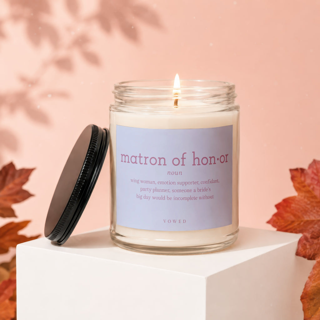 Glass jar candle with lit wick, "Matron of Honor" definition label, and lid.