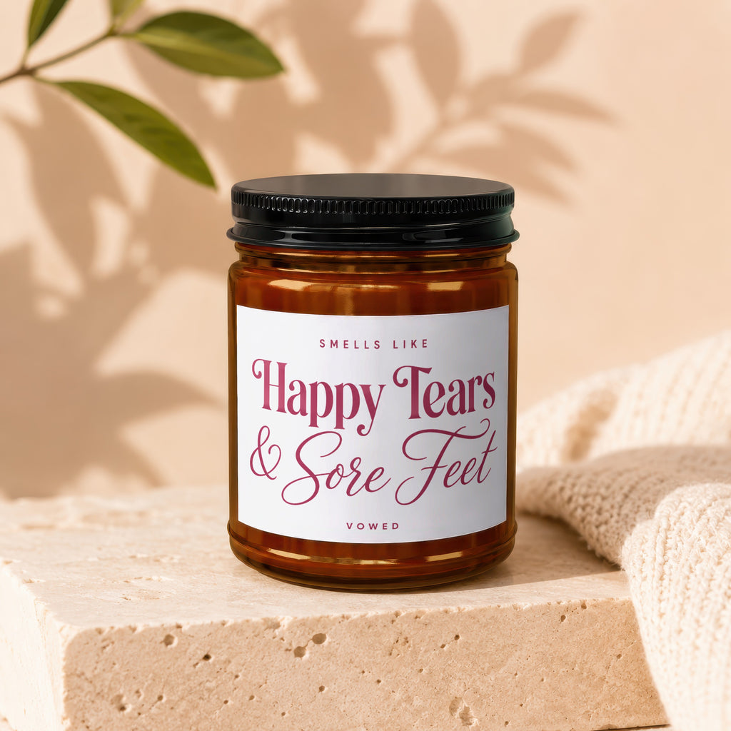 Amber candle in glass jar with black lid labeled "Smells Like Happy Tears & Sore Feet."