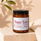 Amber candle in glass jar with black lid labeled "Smells Like Happy Tears & Sore Feet."