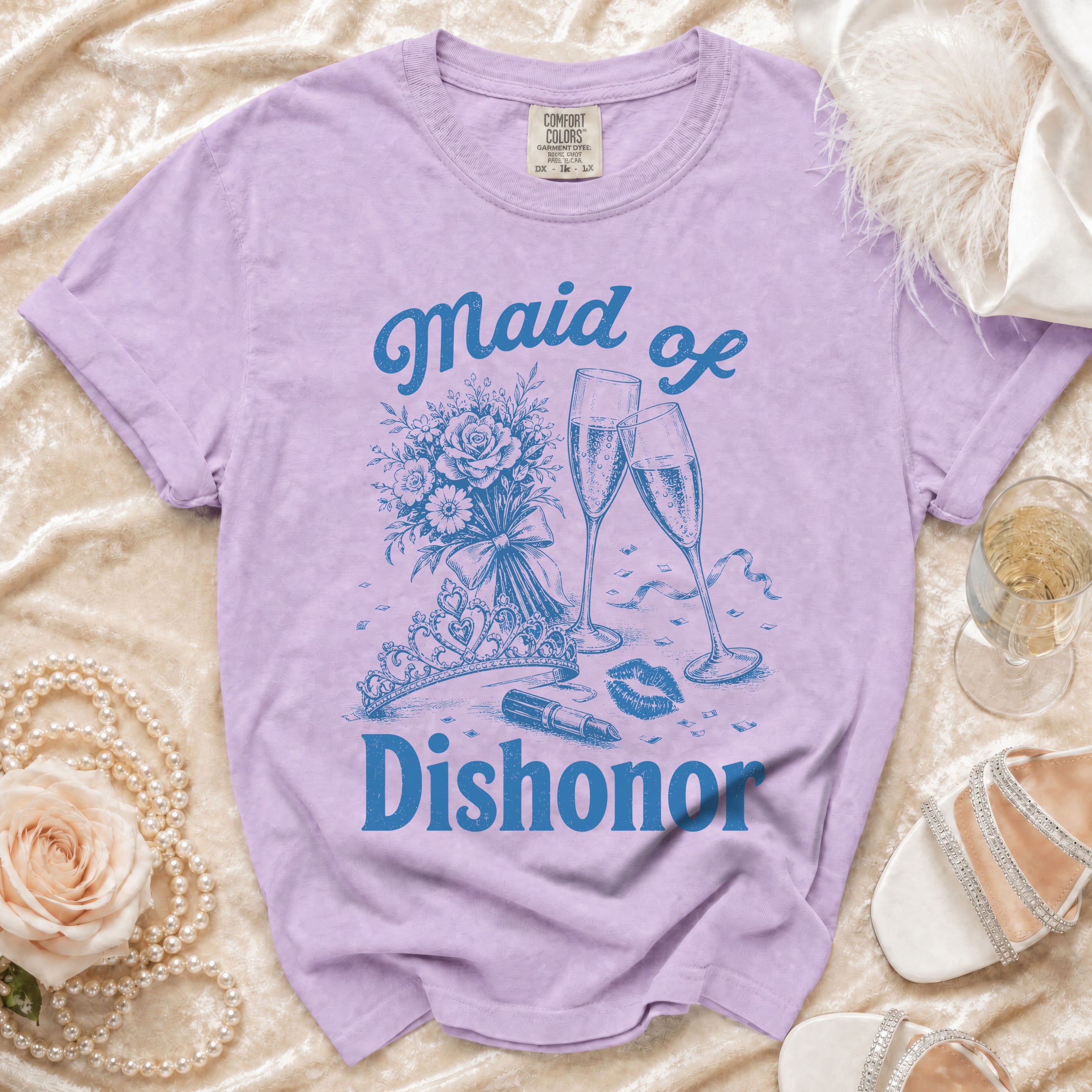 Lavender t-shirt with "Maid of Dishonor" text, champagne glasses, bouquet, tiara, and lipstick.
