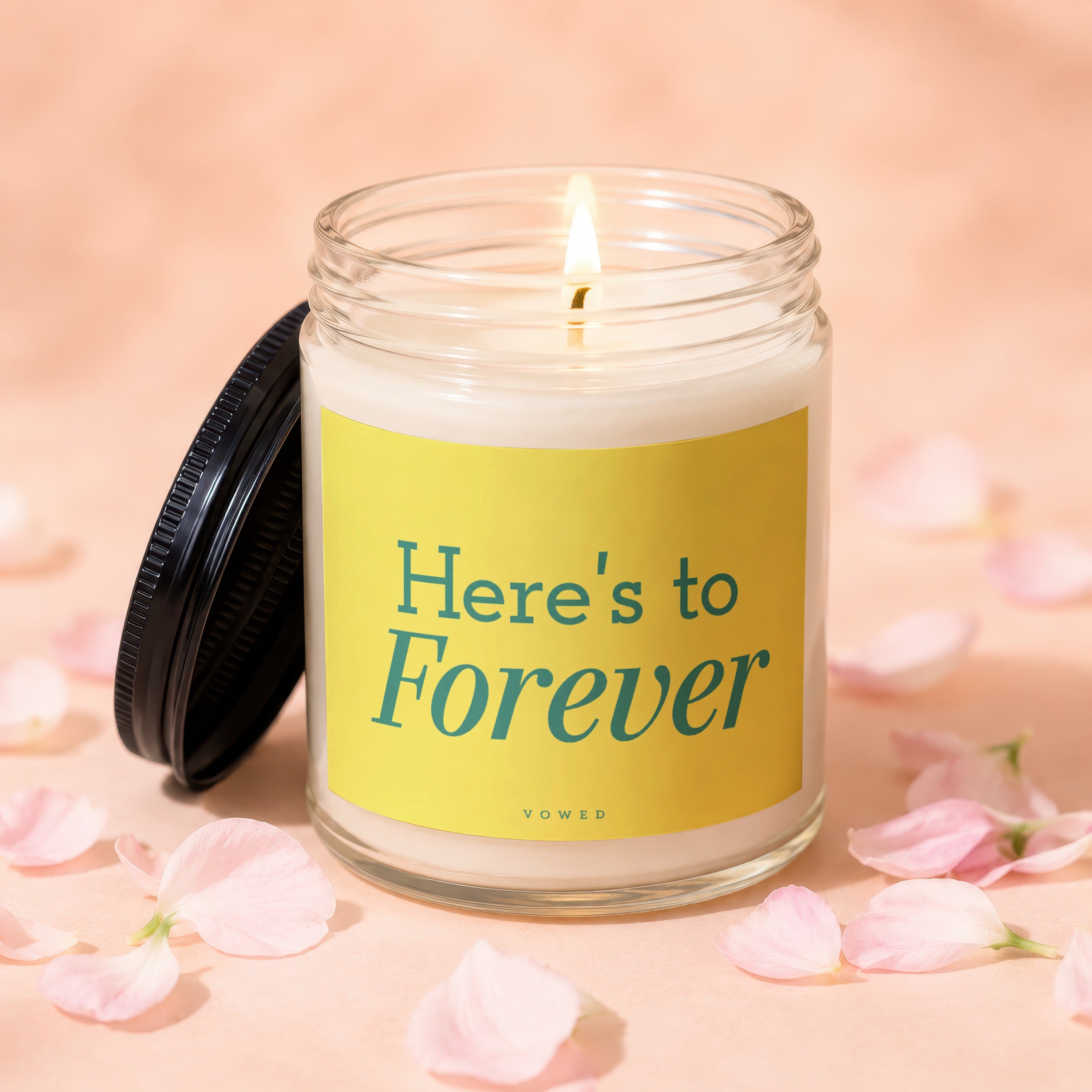 Candle with lit wick, yellow label reads "Here's to Forever"