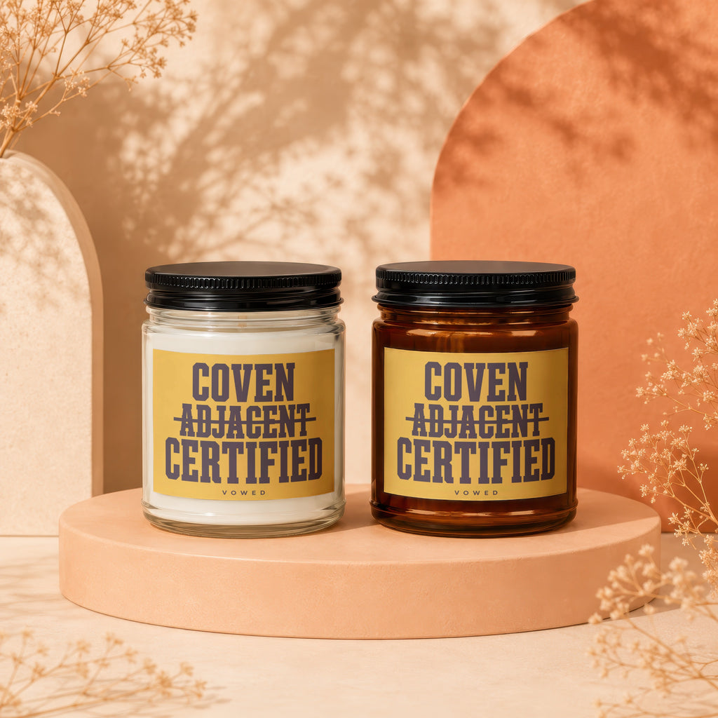 Two candles with yellow labels reading "Coven Adjacent Certified Vowed".