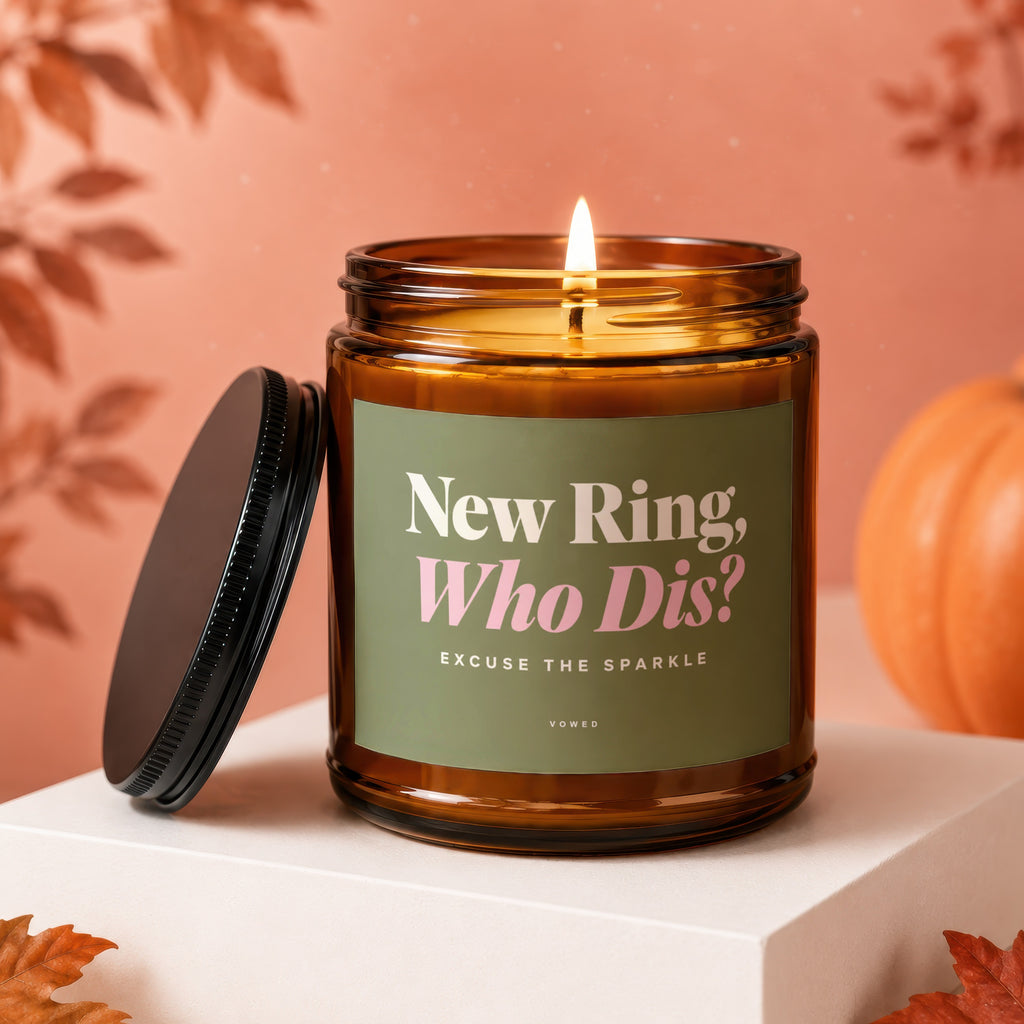 Amber jar candle with a lit wick, black lid, and green label reading "New Ring, Who Dis? Excuse the Sparkle".
