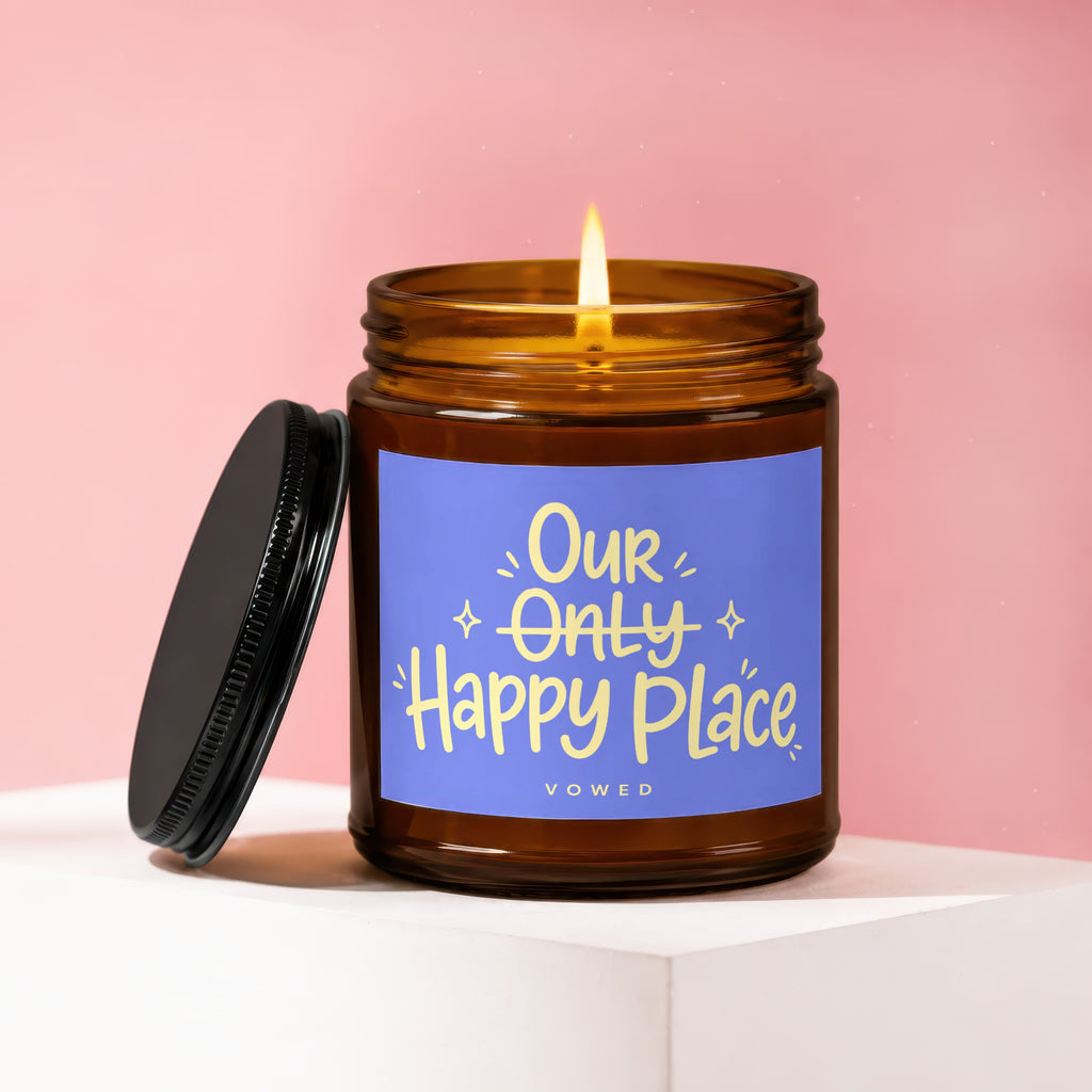Candle with lit flame and purple label reading "Our Only Happy Place"