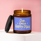 Candle with lit flame and purple label reading "Our Only Happy Place"