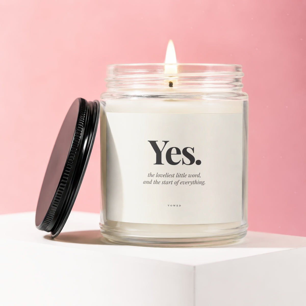 Glass candle with lit wick, "Yes. the loveliest little word, and the start of everything." text.
