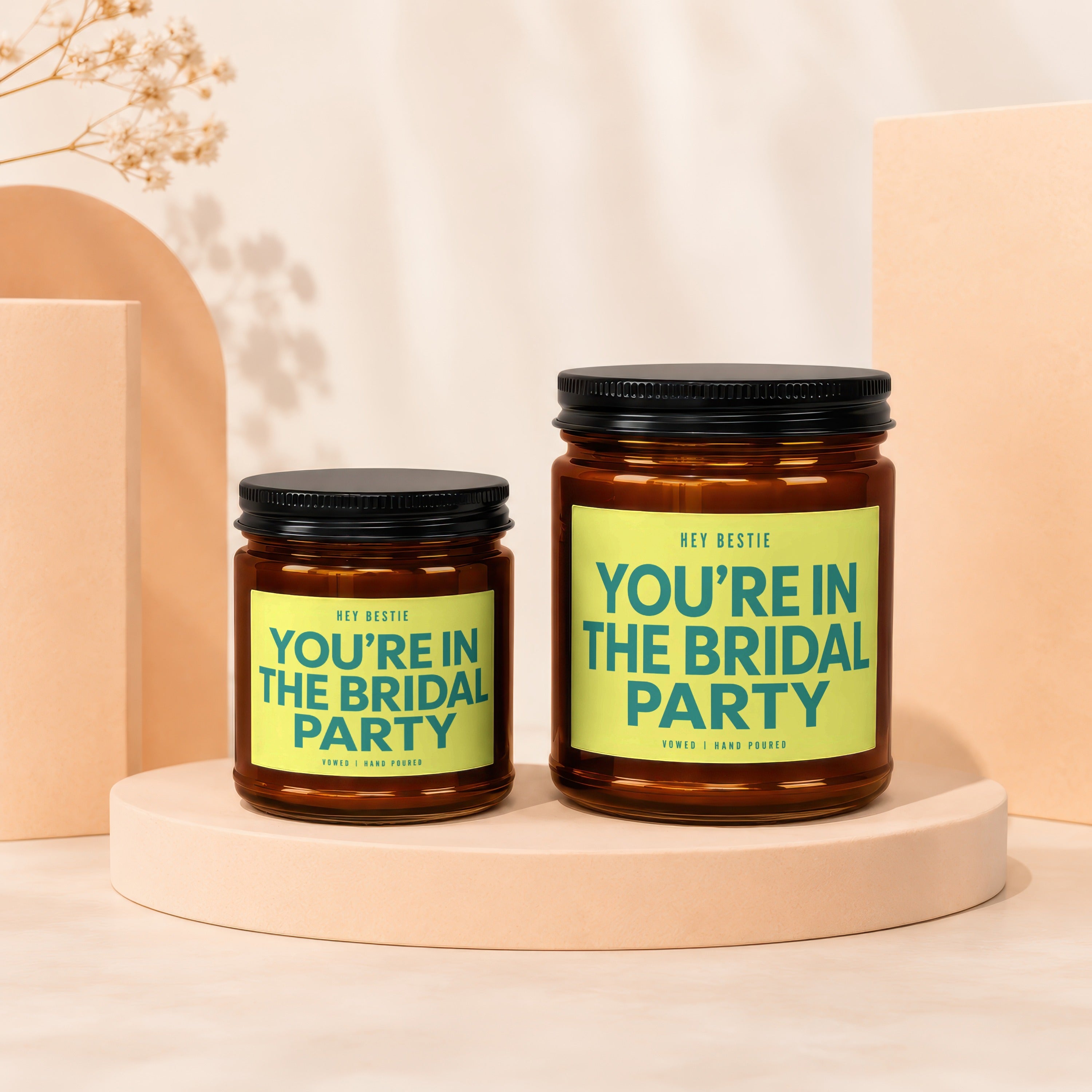 Two amber jars with black lids, featuring bright yellow labels that read "HEY BESTIE YOU'RE IN THE BRIDAL PARTY."