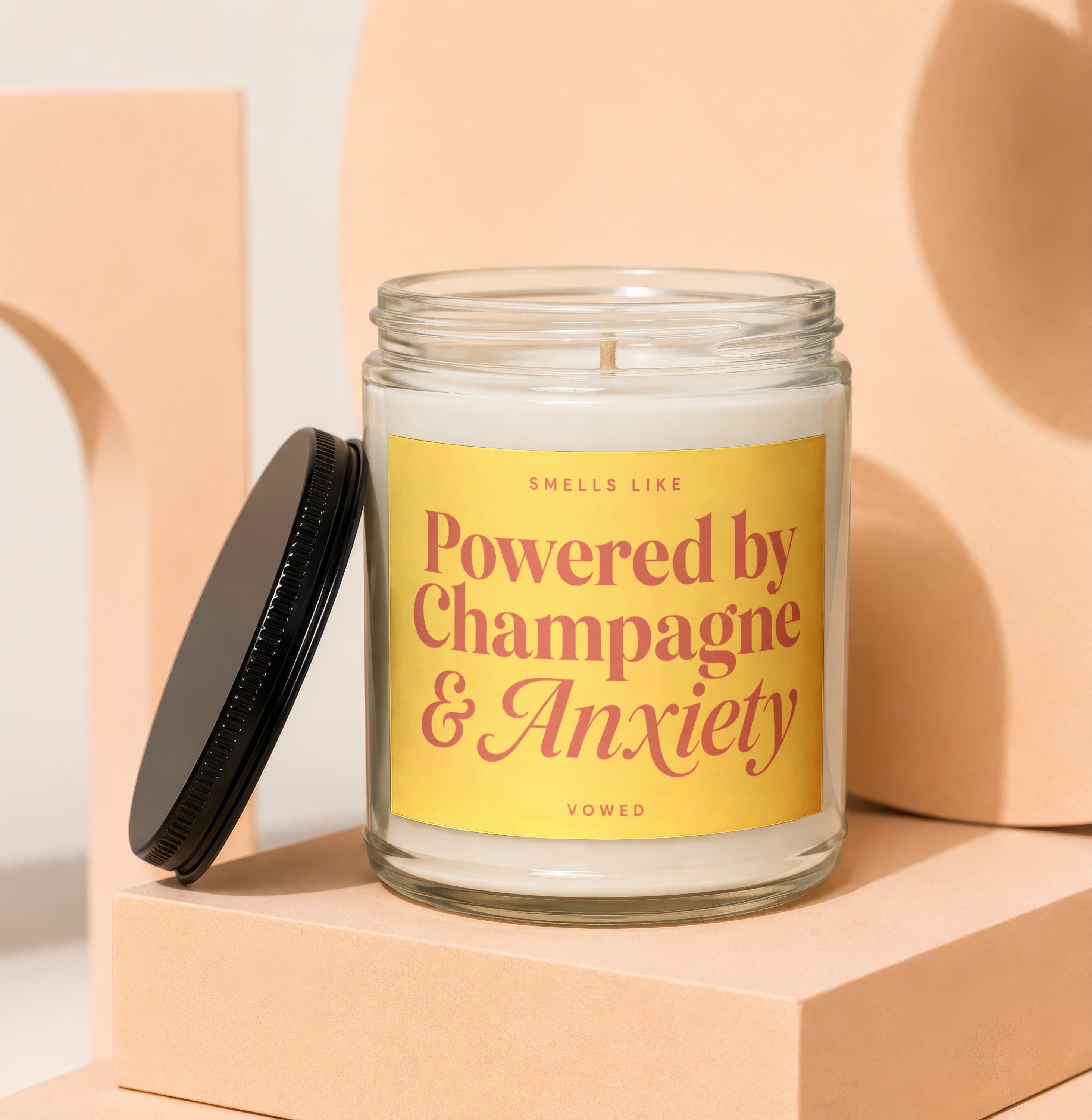 Scented candle in glass jar with black lid, reads "Smells like Champagne & Anxiety".