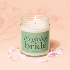 Scented jar candle with text "it's giving bride" surrounded by pink flower petals.