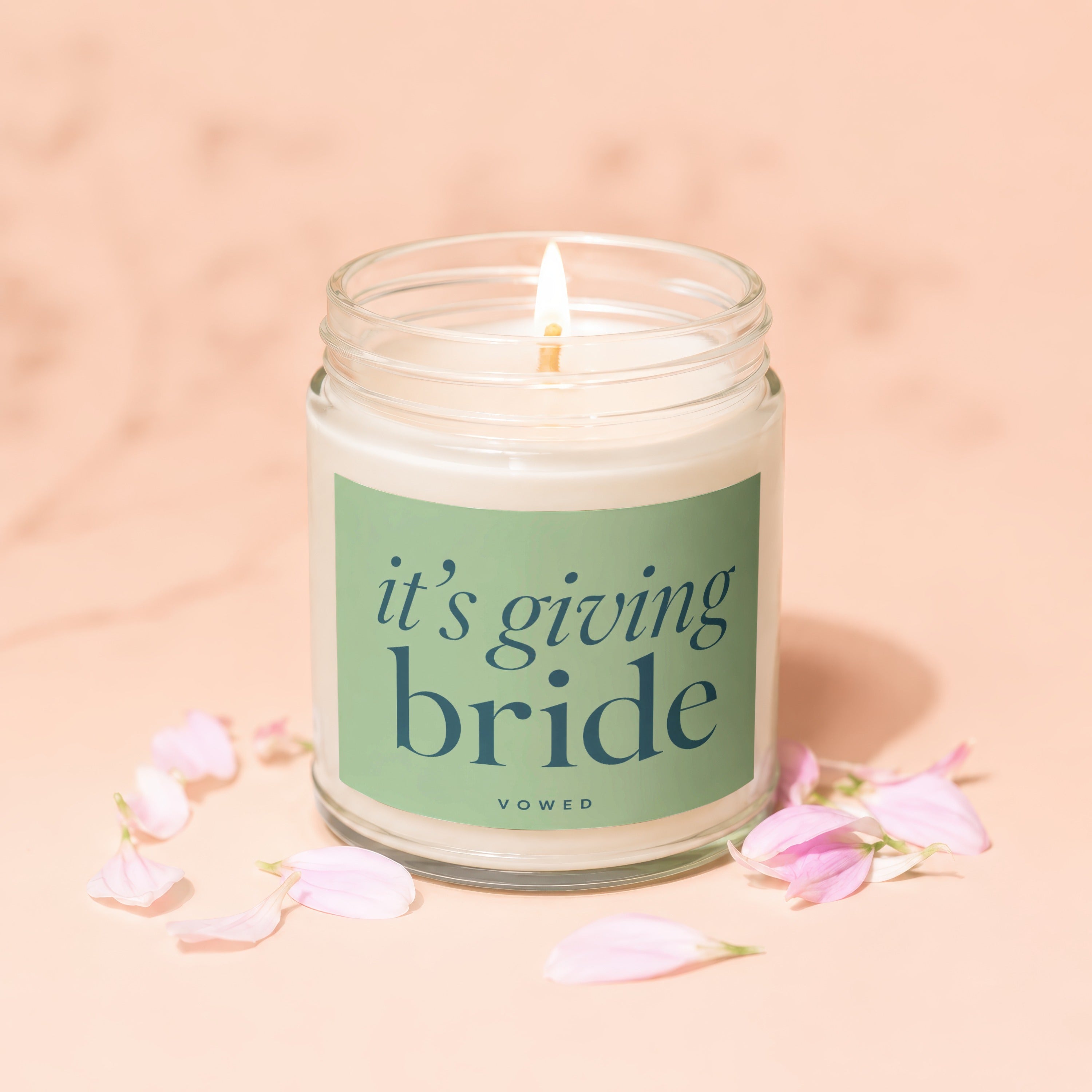 Scented jar candle with text "it's giving bride" surrounded by pink flower petals.