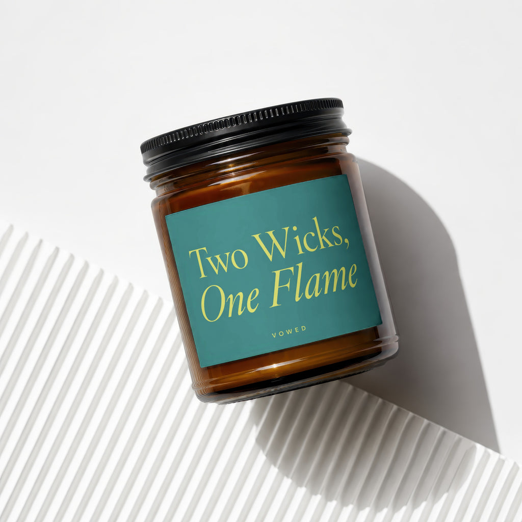Amber jar candle with black lid, teal label reading "Two Wicks, One Flame" and "VOWED".