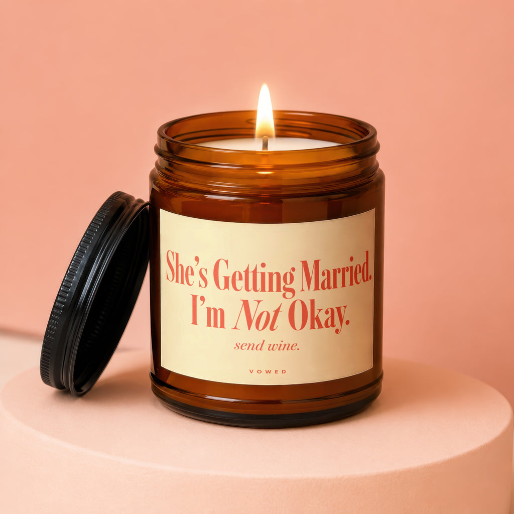Amber candle with lit flame and lid nearby, reads "She's Getting Married. I'm Not Okay. send wine."