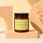 Amber candle with black lid and yellow label reading "It's Not Crying, It's Allergies, It's Love"