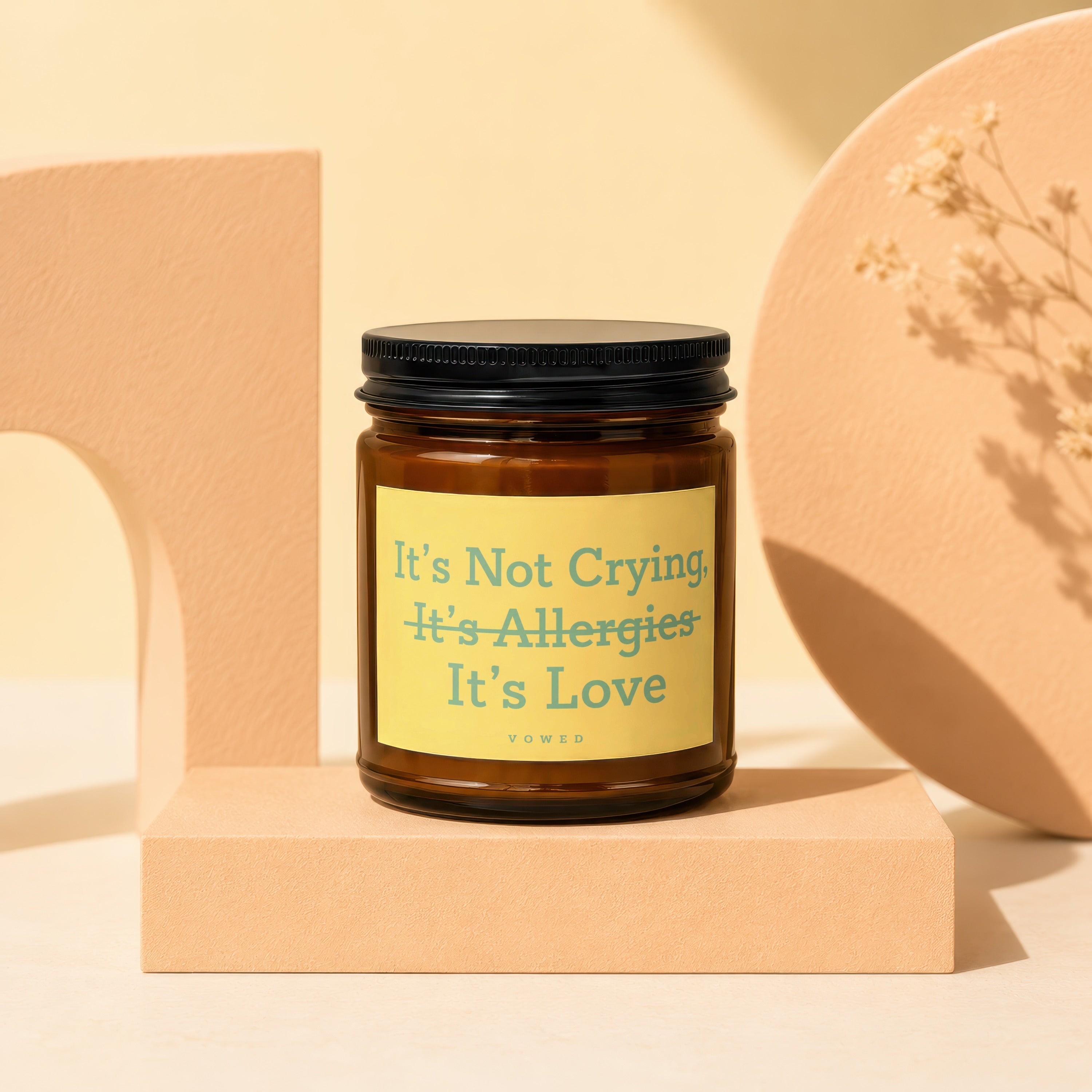 Amber candle with black lid and yellow label reading "It's Not Crying, It's Allergies, It's Love"