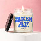 Glass candle with black lid and "TAKEN AF. VOWED." text on cream label with pink background.