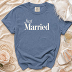 Blue t-shirt with "Just Married" text, on a creamy fabric, with accessories.