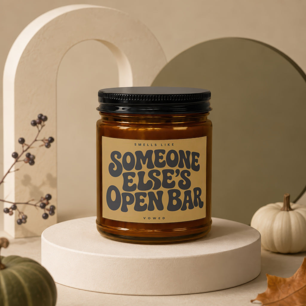 Amber glass candle with black lid, text reads "Smells Like Someone Else's Open Bar, Vowed".