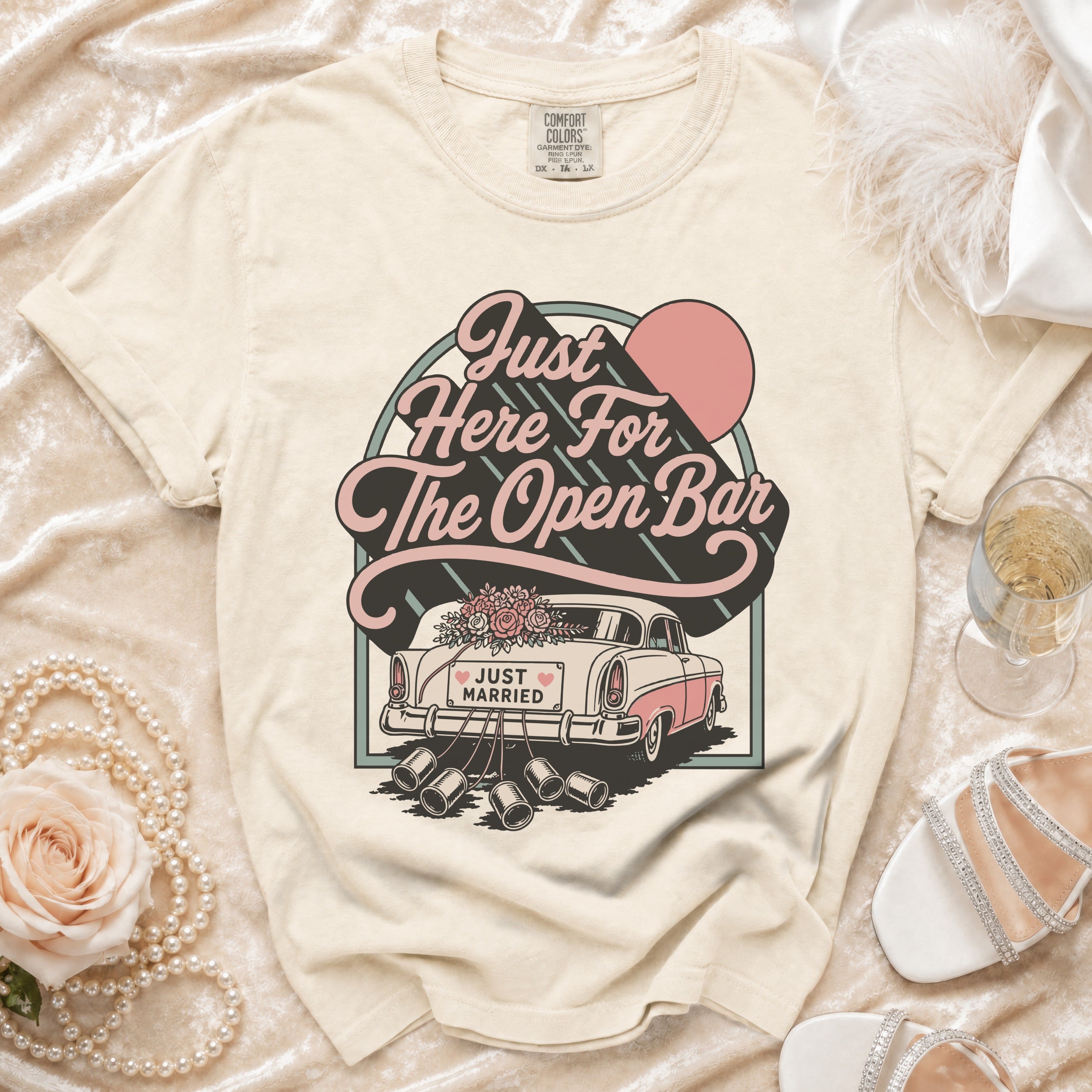 "Just Here For The Open Bar" text with vintage car and wedding cans graphic on cream t-shirt.
