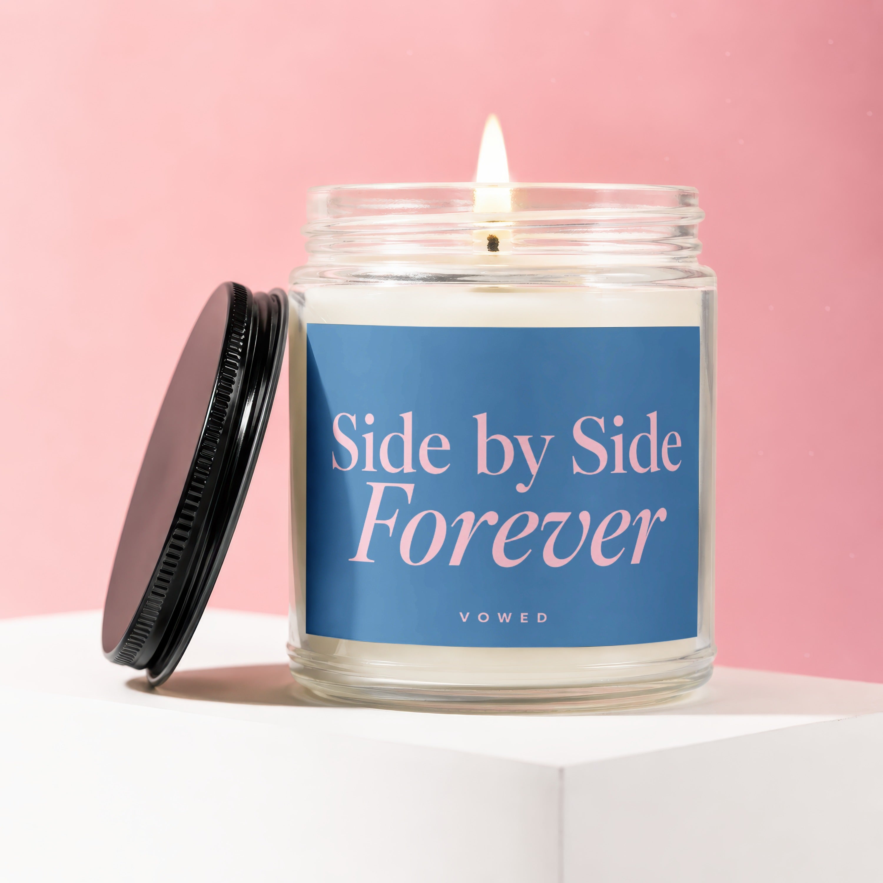 Glass candle with lit wick and blue label reading "Side by Side Forever", Vowed.