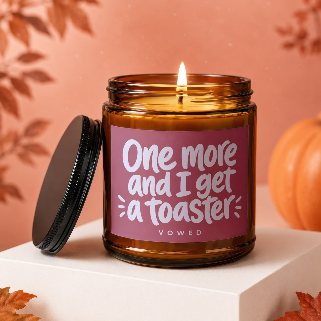 Amber jar candle with lit wick displays text "One more and I get a toaster".