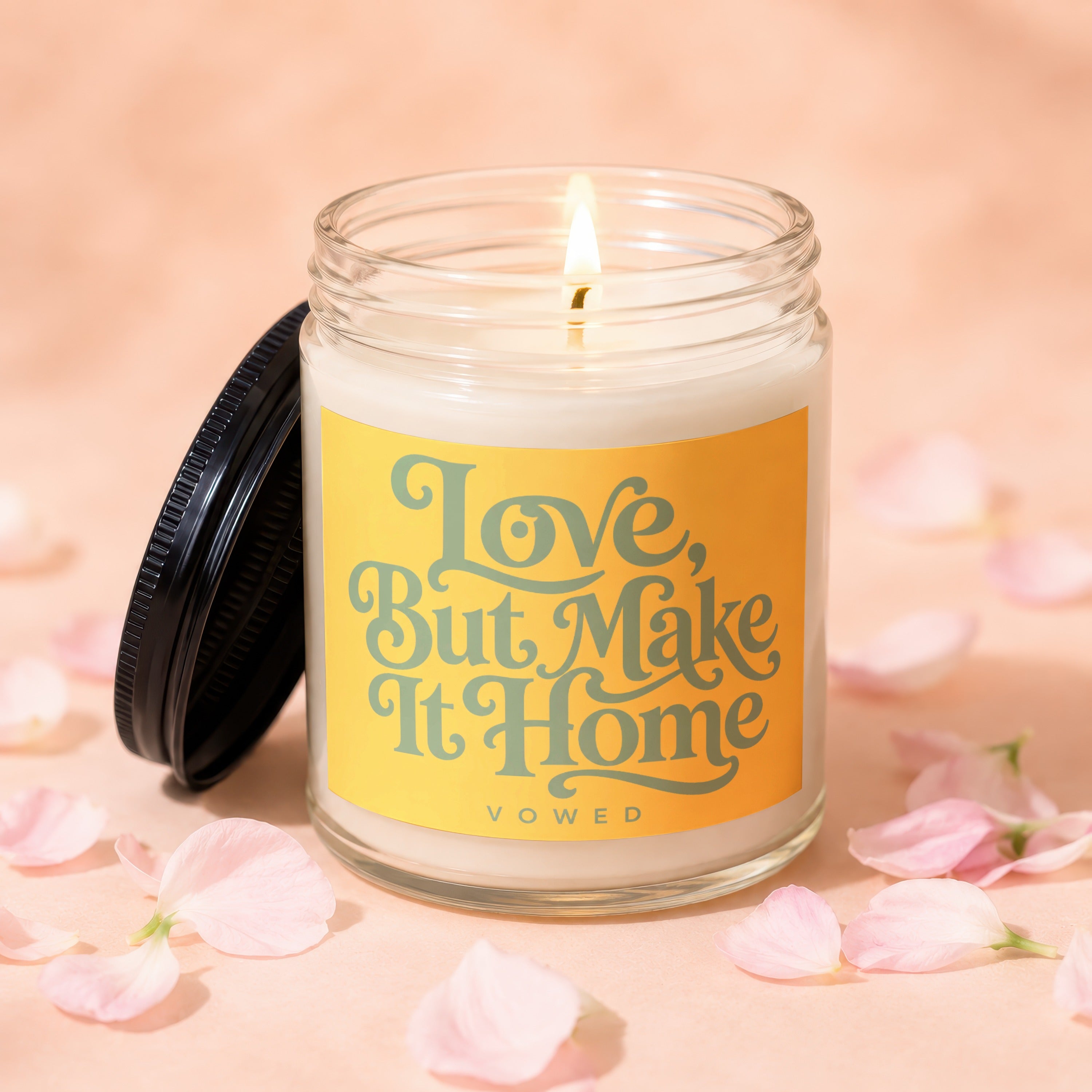 Glass candle with lit wick and "Love, But Make It Home" text on label.